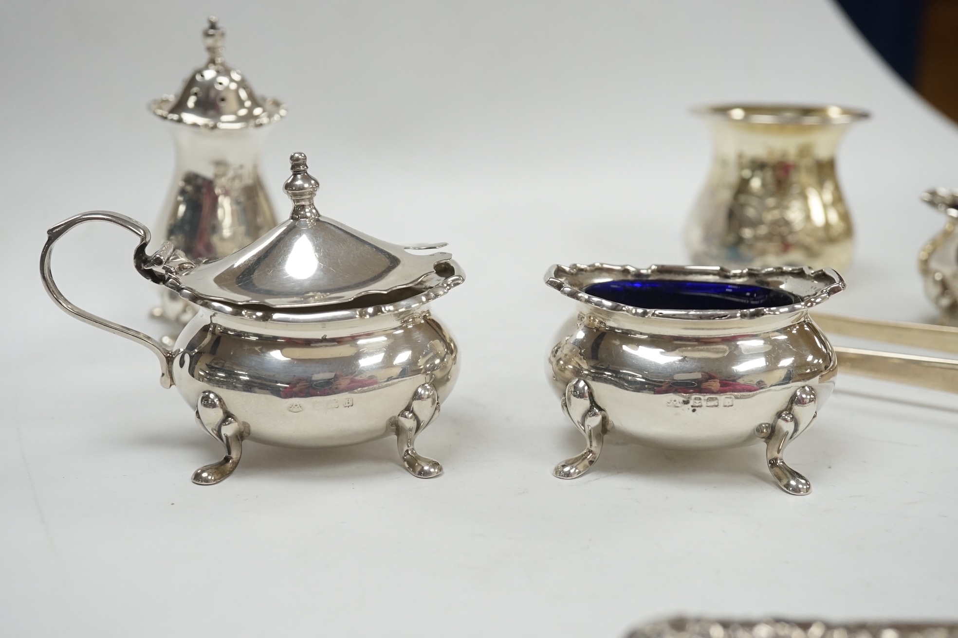 A George V silver four piece condiment set by Adie Bros. Birmingham, 1926 and three other items including a pair of Georgian silver sugar tongs, London 1799. Condition - poor to fair